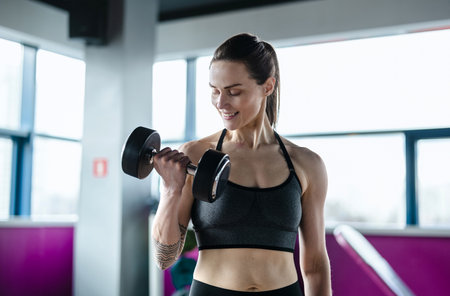 Portrait of smiling young woman lifting dumbbells in fitness studioの写真素材