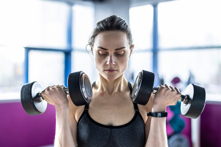 Portrait of a young woman lifting dumbbells at the gymの写真素材