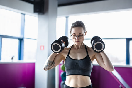 young sporty woman working out with dumbbells in fitness studioの写真素材