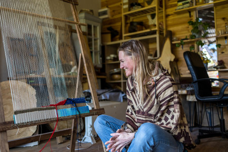 Blond woman sitting in front of a loom in a workshopの写真素材