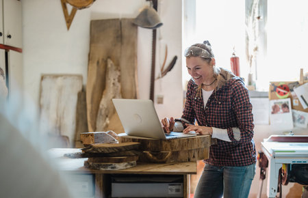 Portrait of smiling female artisan using laptop while working in her workshopの写真素材