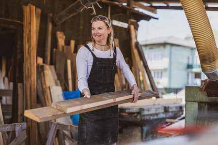 Portrait of confident female carpenter standing with planks in workshopの写真素材