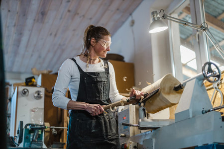 Portrait of mature woman working on woodworking machine in workshop.の写真素材