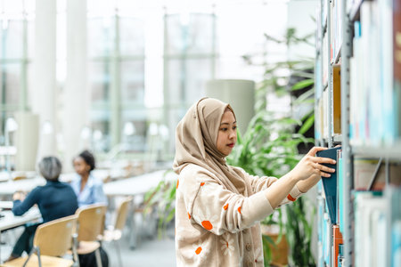 Young asian muslim woman in hijab using mobile phone and working in libraryの写真素材