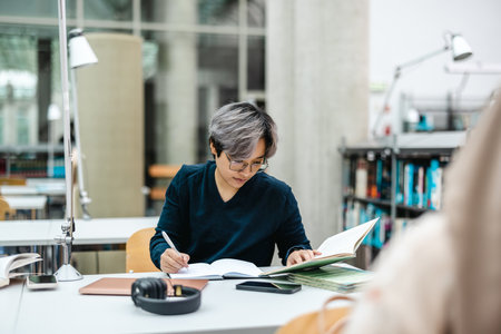 high angle view of mature Asian woman writing in notebook at table in officeの写真素材