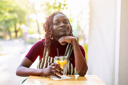 Thoughtful african american woman sitting in cafe with orange juiceの写真素材