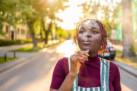 Young african american woman smoking electronic cigarette in the street.の写真素材