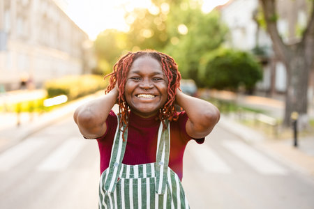 cheerful african american woman with dreadlocks in apron on streetの写真素材