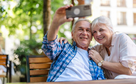Happy senior couple taking selfie with smartphone while sitting on bench in cafe