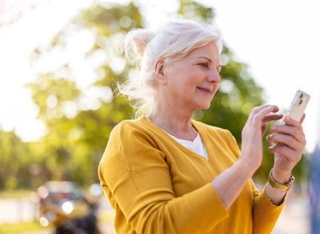 smiling senior woman with smartphone in park on summer day, outdoorsの写真素材