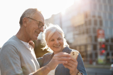 Senior couple using mobile phone in the city. They are looking at the smartphone screen and smiling.の写真素材