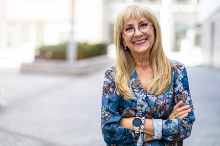 Portrait of happy senior woman with arms crossed standing in city streetの写真素材