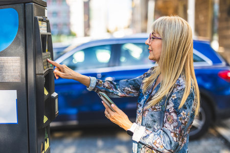 Young blonde woman using a mobile phone to pay for parking in the cityの写真素材