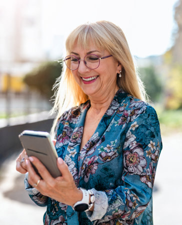 Portrait of a smiling senior woman using mobile phone in the streetの写真素材