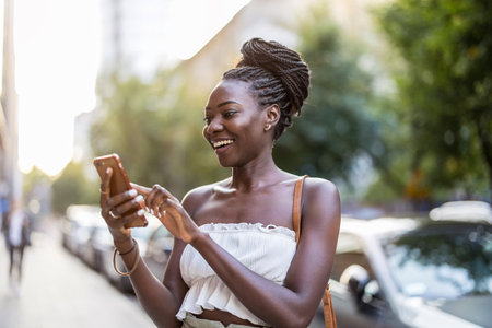 Portrait of smiling African woman using mobile phone in the cityの写真素材