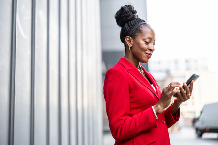 african american businesswoman in red suit with mobile phone in cityの写真素材