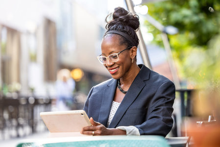 happy african american businesswoman using tablet computer in outdoor cafeの写真素材