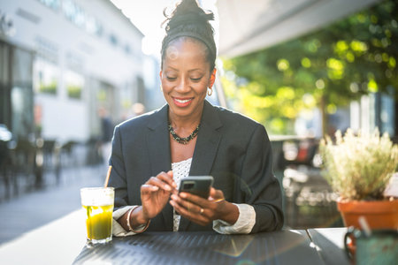 Portrait of smiling businesswoman using mobile phone while sitting in cafe outdoorsの写真素材