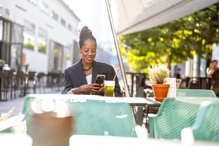 Portrait of a smiling businesswoman using mobile phone in outdoor cafeの写真素材