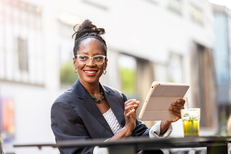 Portrait of happy african businesswoman using tablet computer in outdoor cafeの写真素材