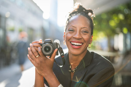 Portrait of smiling african american woman holding camera in cityの写真素材