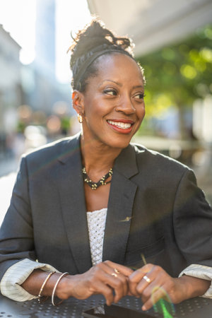 Portrait of a smiling businesswoman sitting at a table in the streetの写真素材