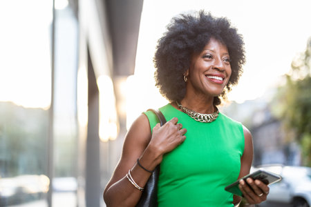 Portrait of smiling african american woman with mobile phone in the cityの写真素材