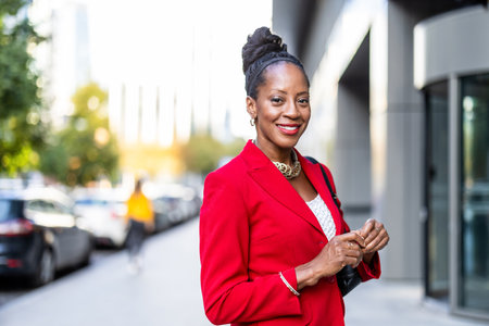 Portrait of a smiling african american businesswoman in red jacket walking outdoorsの写真素材