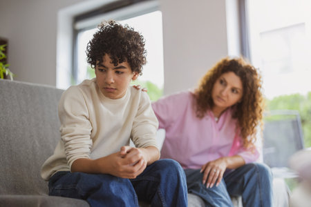 Upset mother and son sitting on sofa in living room at homeの写真素材