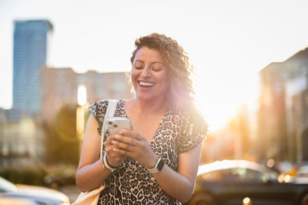 Portrait of smiling young woman using mobile phone while standing in cityの写真素材