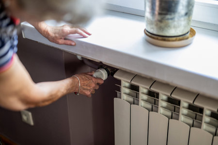 Senior woman adjusting thermostat on the radiator in the living roomの写真素材
