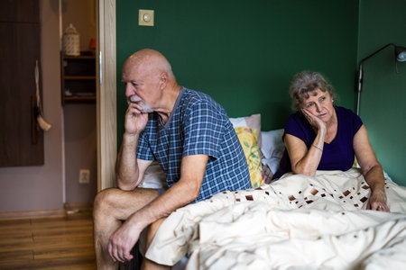 Senior couple having a dispute while sitting on the bed in the bedroomの写真素材