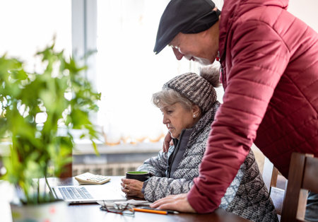 Elderly couple using a laptop in winter clothing at homeの写真素材