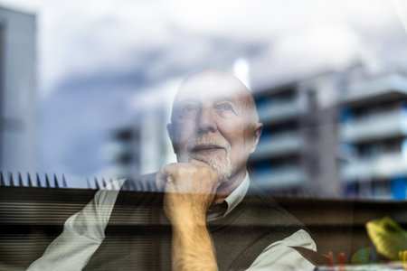 Portrait of thoughtful senior man looking through window with city in backgroundの写真素材