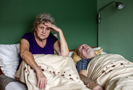 Elderly woman with headache and her husband lying on the bedの写真素材