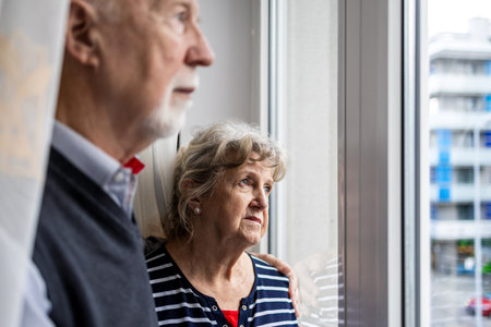 Portrait of senior couple looking out the window while standing at homeの写真素材
