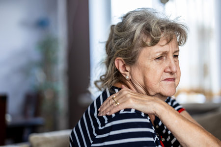 Portrait of senior woman suffering from neck pain while sitting on sofa at homeの写真素材