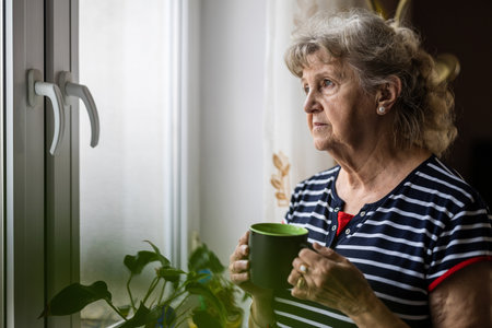 Elderly woman with cup of tea near the window at homeの写真素材