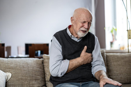 Senior man suffering from shoulder pain while sitting on sofa at home.の写真素材