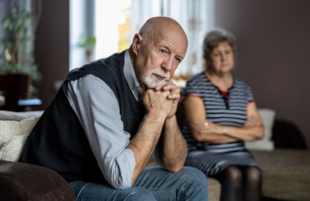 Upset senior couple sitting on sofa in living room at homeの写真素材