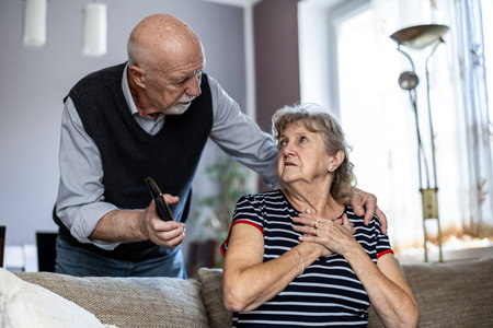 Senior couple using mobile phone while sitting on sofa in living room at homeの写真素材
