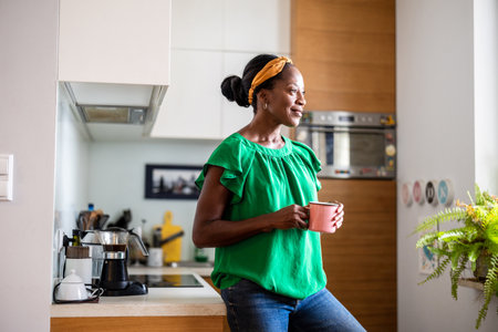 african american woman with cup of coffee in kitchen at homeの写真素材