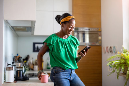 african american woman using mobile phone in the kitchen at homeの写真素材