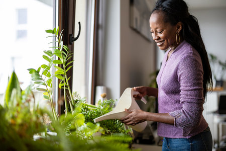 african american woman watering houseplants at home in sunny dayの写真素材
