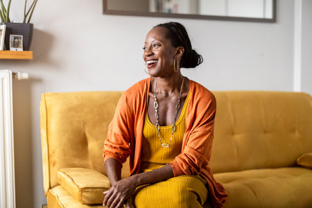 portrait of beautiful young african woman smiling while sitting on sofa at homeの写真素材