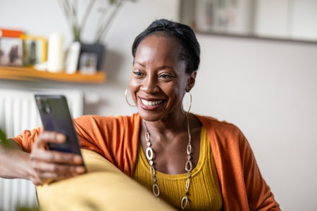 Portrait of smiling african american woman using mobile phone at homeの写真素材