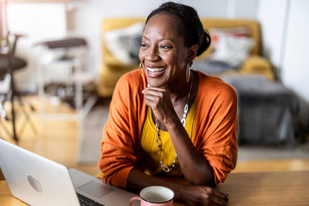 Portrait of smiling senior woman using laptop in living room at homeの写真素材