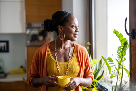 Portrait of smiling senior woman holding cup while standing in kitchen at homeの写真素材