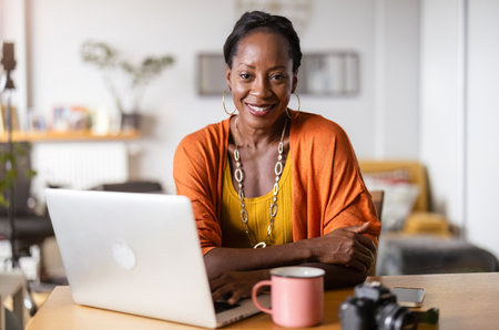 Portrait of smiling mature woman using laptop in coffee shop. Mature businesswoman working from home.の写真素材