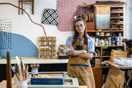 Portrait of confident female artist standing with arms crossed in her workshopの写真素材